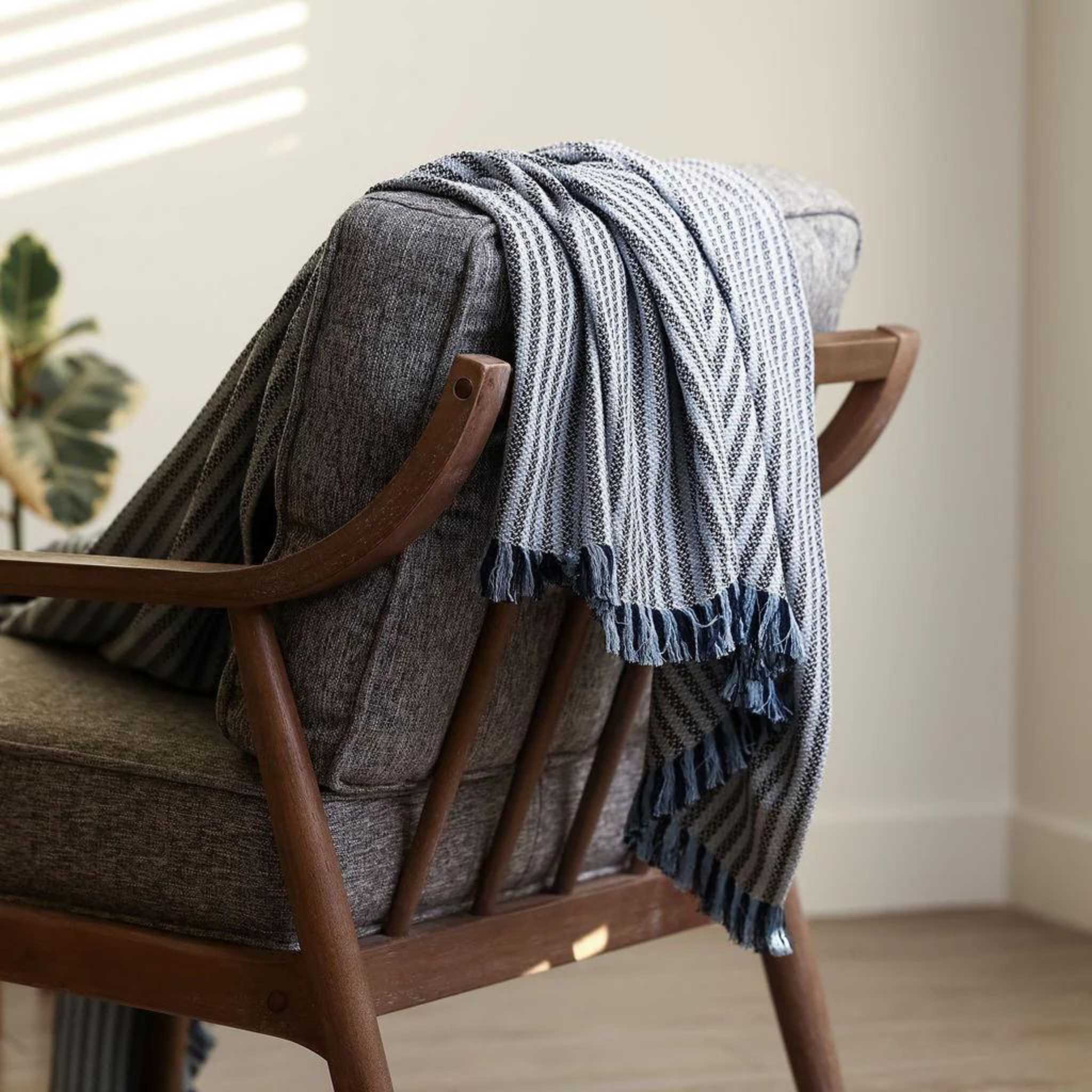 boucle's 100% cotton throw blanket with navy blue stripes across it is styled over a chair sofa