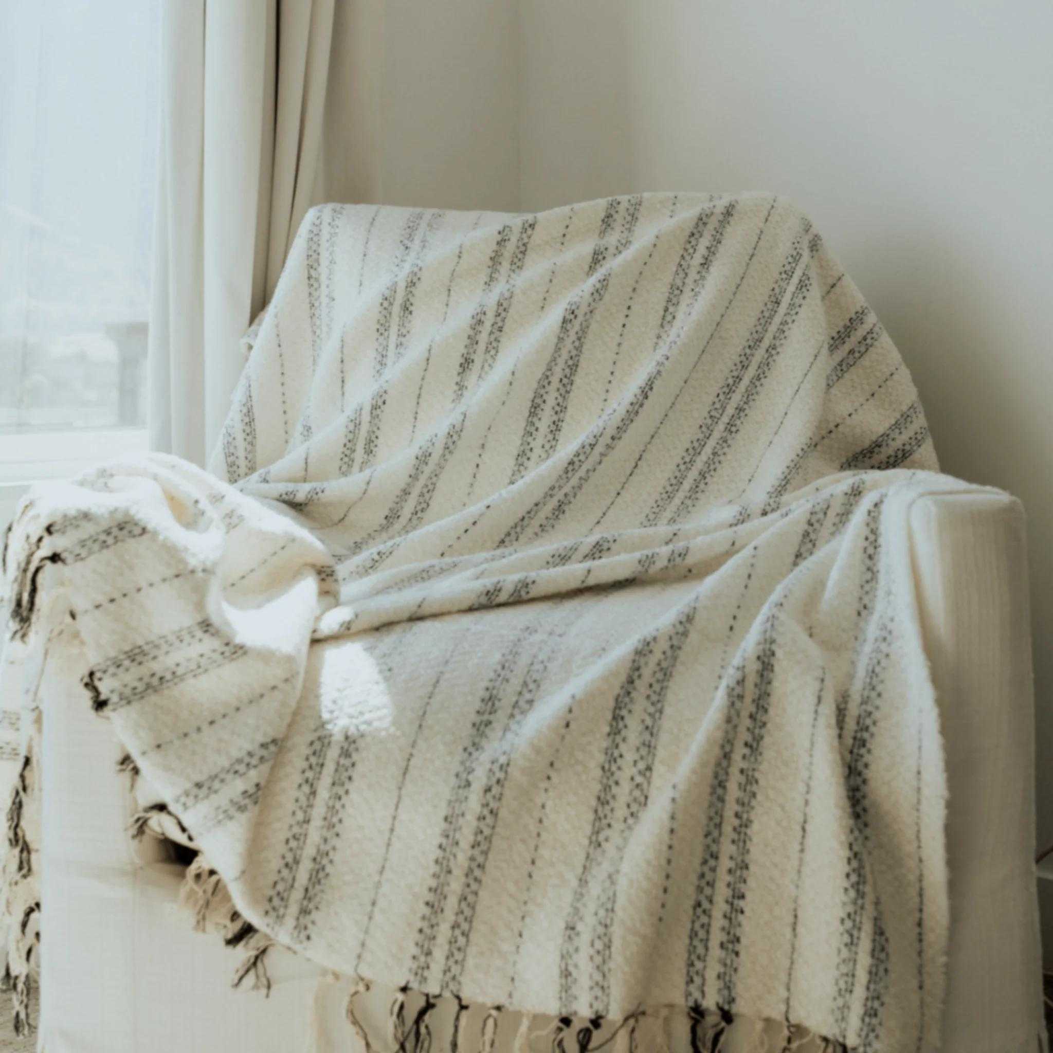 a soft white and black tweed throw blanket styled over a white sofa