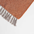 corner view of our burnt orange throw blanket showing the style of the edge with grey tassels