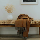 elegantly styled modern boho orange throw blanket with grey tassels over a bench