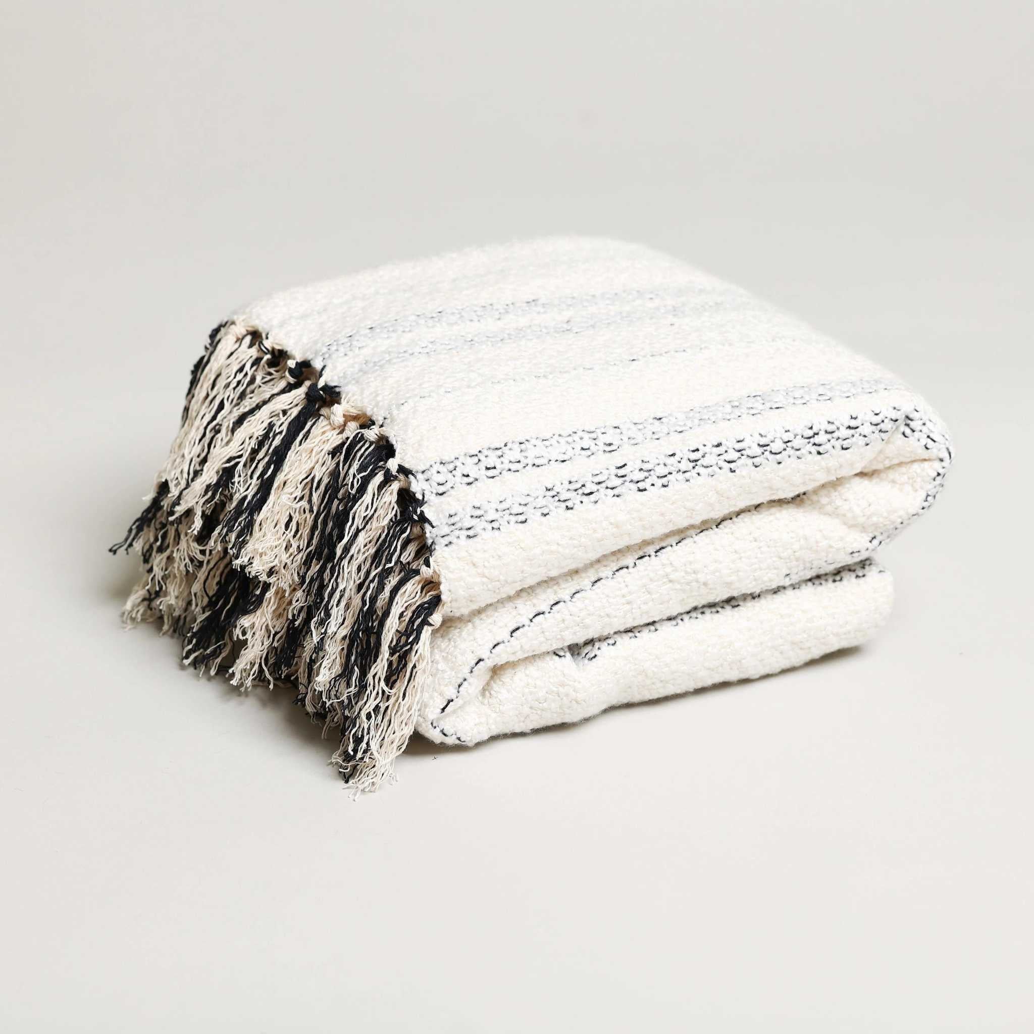 white folded throw blanket with black stripes and tassels