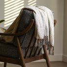 white cream colored throw blanket styled over a couch with uniquely designed tassels and pattern striped